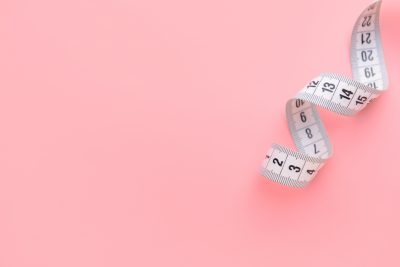 White measuring tape isolated on a light pink background