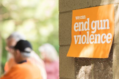 An orange sign reading "We can end gun violence." In the background is a group of people wearing orange gun violence awareness t-shirts.