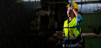 Tired female worker wearing a hard hat wipes sweat off her face. 