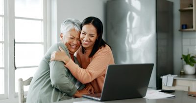 Mother and her adult daughter are looking at a laptop screen and hugging