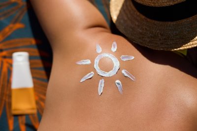 Person tans outside. On their shoulder is the outline of a sun made with sunscreen