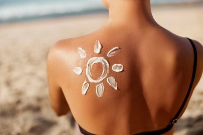 A woman applies sunscreen in the shape of a sun on her shoulder