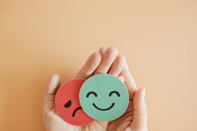 Hands holding wooden blocks depicting a sad face and smiling face